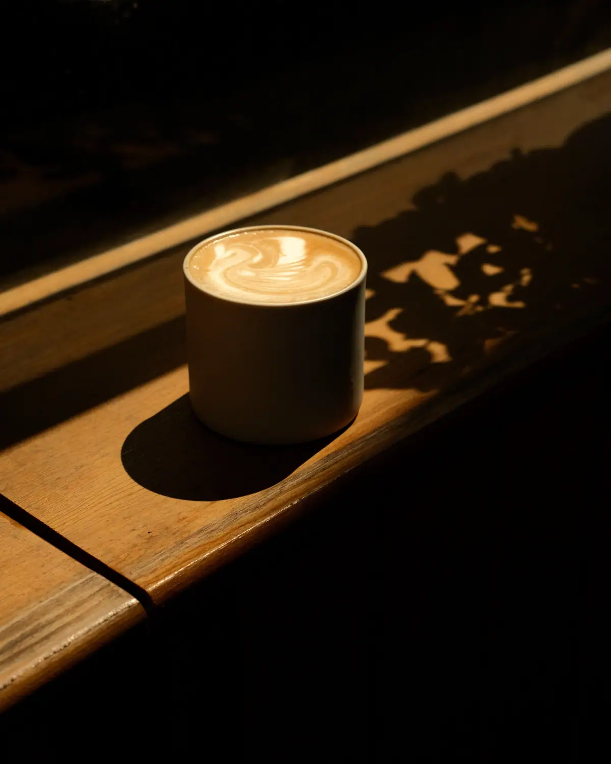 Un latte cu rozetă pe pervazul de lemn, în lumina de după-amiază